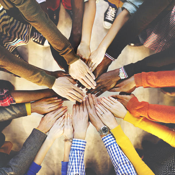 People standing in circle extending arms out to place hands on each others